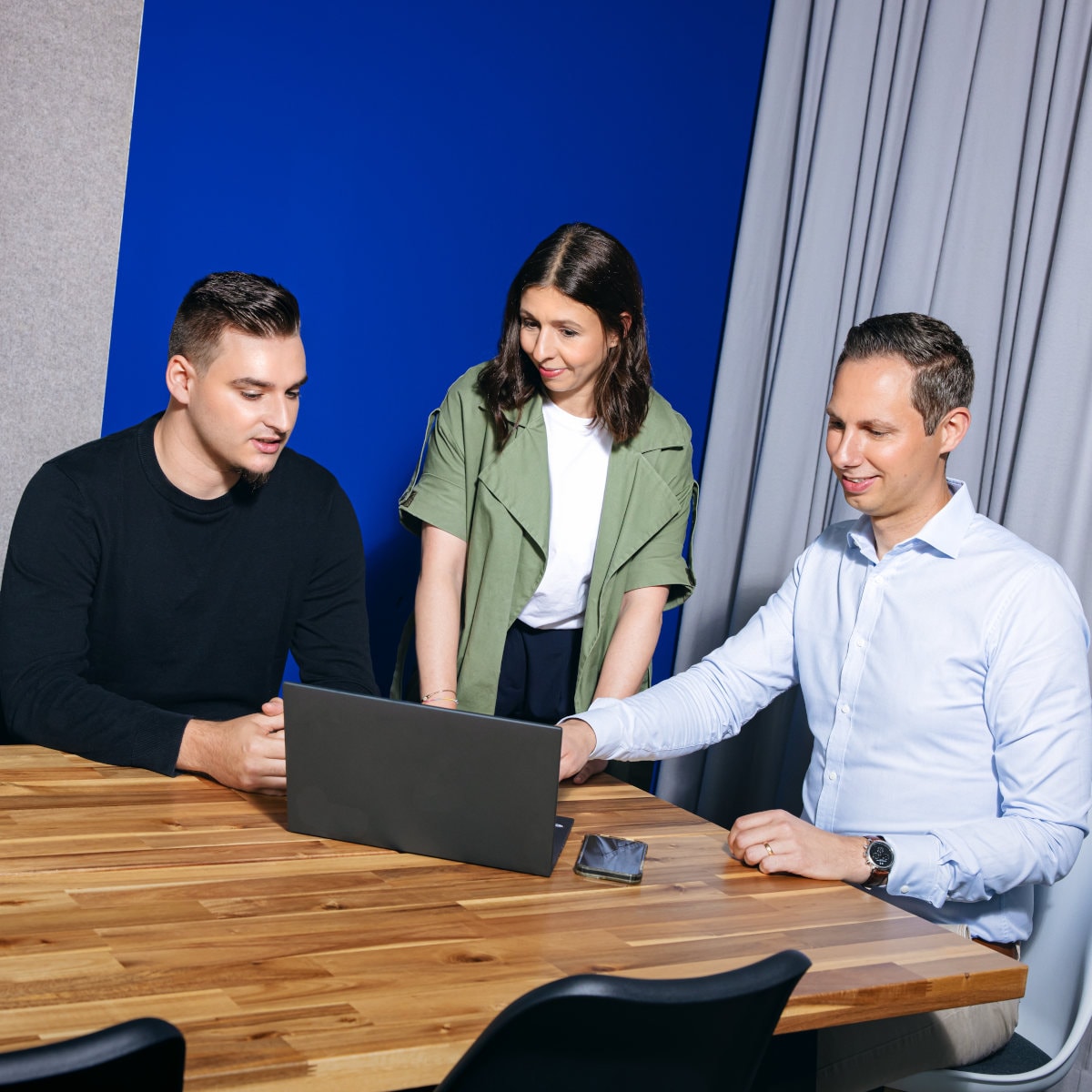 Drei Teammitglieder arbeiten gemeinsam an einem Konferenztisch und sehen sich während einer Besprechung Informationen auf einem Laptop an