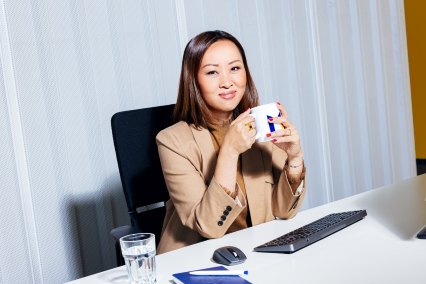 a person sitting at a desk holding a mug and smiling